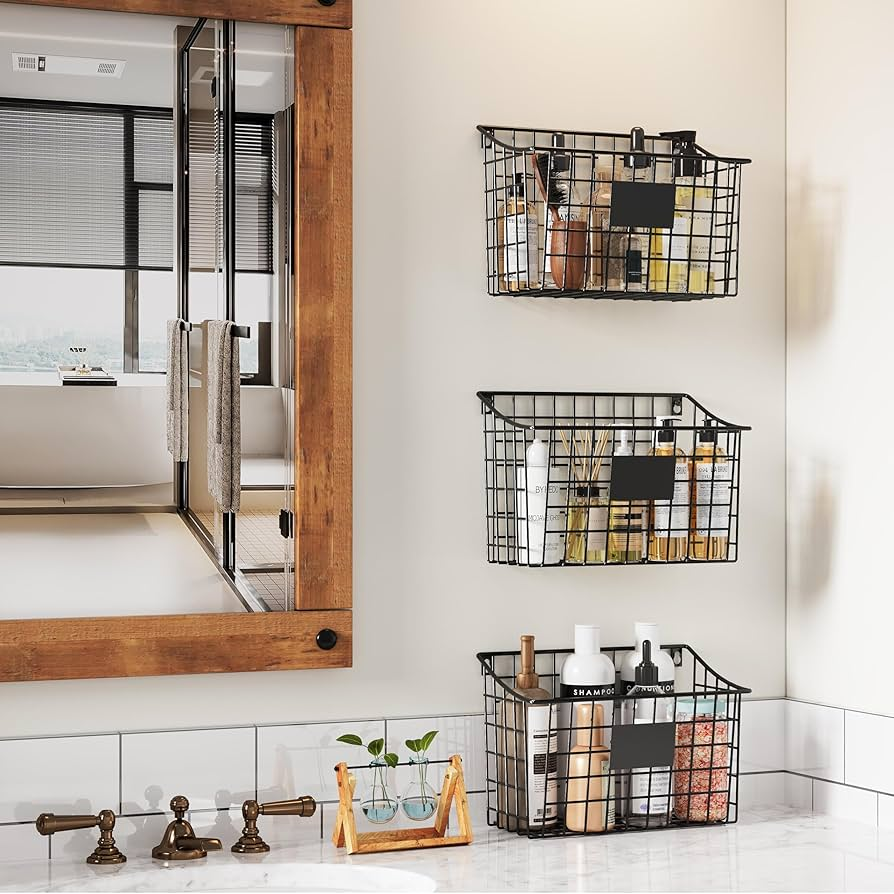 Wire baskets with toiletries on a bathroom wall, wooden mirror frame, clear sink, test tube plant display, and a city view through blinds.