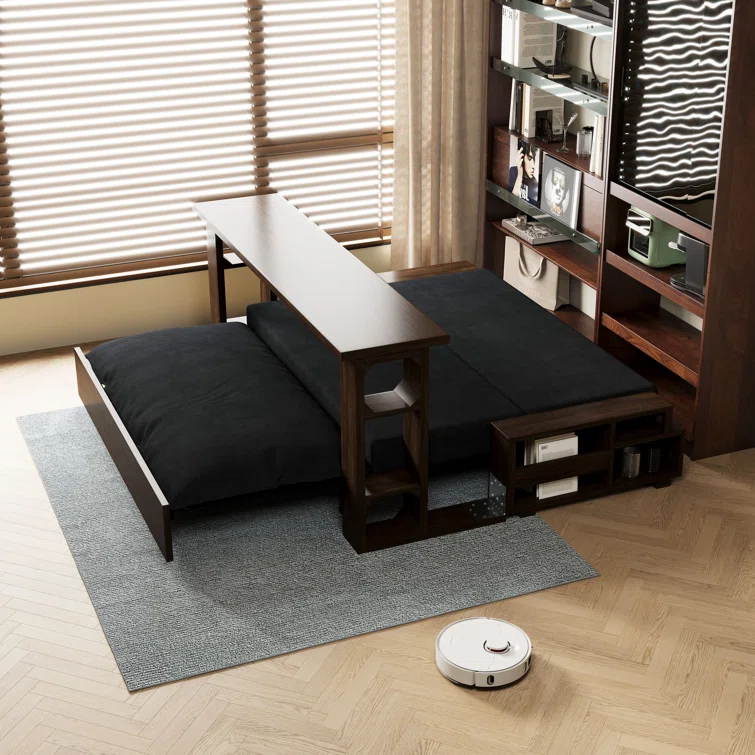 Minimalist living room with dark wooden furniture, black cushions, a gray rug, shelves with books, and a white robot vacuum on hardwood floor.