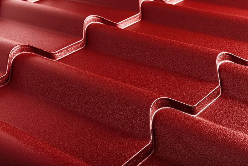 Close-up of red, wavy metal roofing sheets with a glossy finish, showing detailed texture and shadows in a well-lit setting.