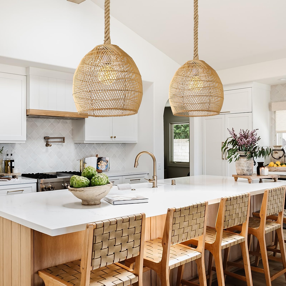 Modern kitchen with a white island, wooden chairs, rattan pendant lights, and decor including artichokes and flowers. Bright, airy atmosphere.