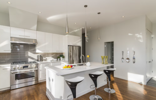 Modern kitchen with white cabinets, stainless steel appliances, fruit bowl on the island, and sleek bar stools. Bright and orderly ambiance.