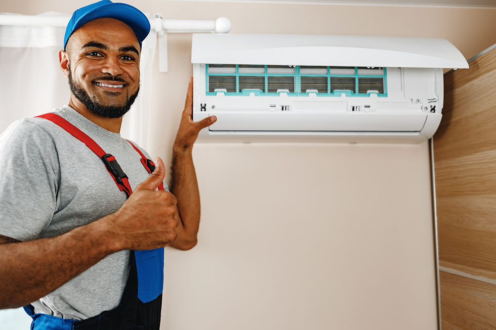 Smiling technician in gray and red uniform giving a thumbs up next to an air conditioner unit indoors. Beige walls and wooden accents.