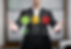 Man in suit presenting feedback icons: green smiley, yellow neutral, red sad. Green checked. Background shows blurred office setting.