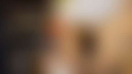 Colorful rooster on a wooden perch by a rustic coop. Background features out-of-focus dishes and kitchen items. Vibrant, lively setting.