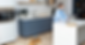 Woman in blue sweater works on laptop in modern kitchen. Brown dog lies on floor. Minimalist decor with blue cabinets and potted plant.
