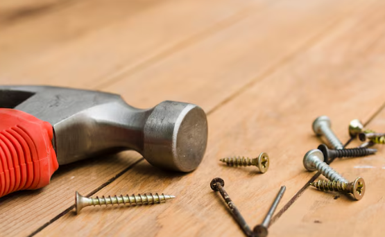 Hammer with a red handle and scattered screws on a wooden surface. Close-up view, highlighting tool and hardware details.