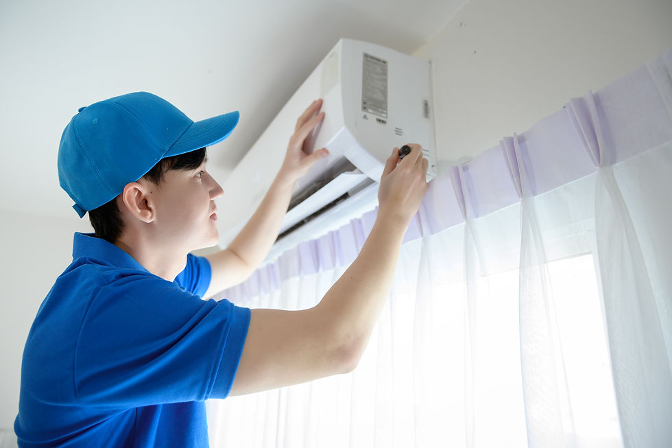 Man in blue cap and shirt installs an air conditioner near white curtains, focused expression. Bright indoor setting.