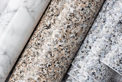 Rolls of marble and granite patterned wallpaper in white, brown, and gray, tightly aligned. The setting is neutral, focusing on textures.
