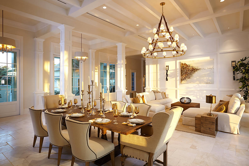 Elegant dining and living room with beige chairs, wooden table set for dining, golden decor, large chandelier, and soft lighting.