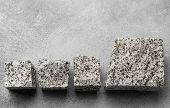 Four granite blocks of varying sizes are lined up on a gray textured background, showcasing different patterns and shades of gray.