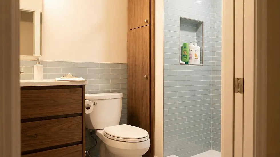 Modern bathroom with wood cabinet, white toilet, and blue tile walls. Shower niche holds shampoo bottles. Clean and minimal design.