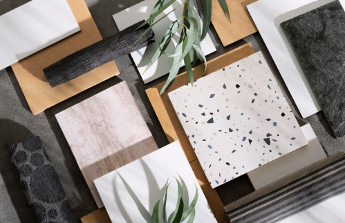 Various textured tiles and swatches in neutral tones are arranged on a surface. Eucalyptus leaves add a natural touch.