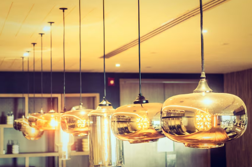 Hanging golden pendant lights in a row illuminate a modern interior with warm wooden tones, reflecting a cozy, elegant ambiance.