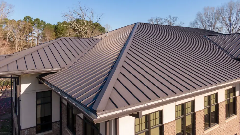 Brown metal roof on a modern beige and brick building. Clear blue sky with bare and evergreen trees in the background.