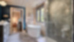 Bathroom with a freestanding tub, glass shower, and dark blue walls. Light wood paneling and "Bienvenue" sign create a cozy ambiance.