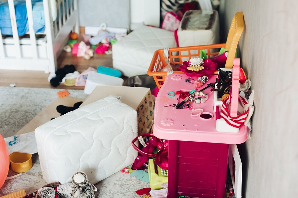 Messy room with scattered toys, pink play kitchen, white mattress. Background shows a bed and colorful clutter, creating a chaotic vibe.