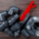 Gray PVC pipe fittings and a red valve on a brown wooden surface. The fittings are neatly arranged, showcasing industrial materials.
