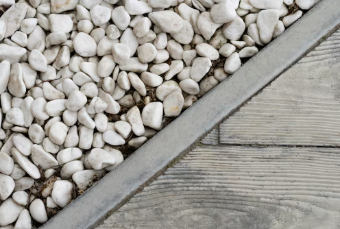 White pebbles arranged on one side, separated by a concrete border, with wooden planks on the other side. Gray and natural tones.