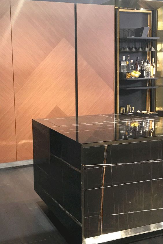 A sleek and modern kitchen island with a black marble countertop and wood paneling. The gold accents and geometric patterns add a touch of luxury and sophistication to the design.