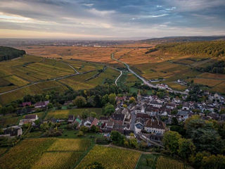 Vue aérienne d’un village entouré de vignes, sous une lumière de fin de journée.