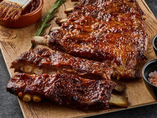 Travers de porc grillés laqués à la sauce barbecue sur planche en bois, avec romarin et sel rose.