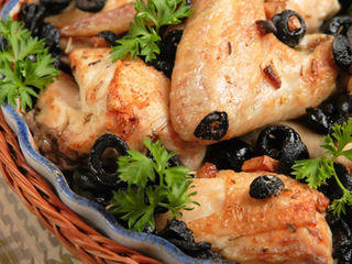 Morceaux de poulet rôti garnis d’olives noires et de persil, servis dans un plat tressé.