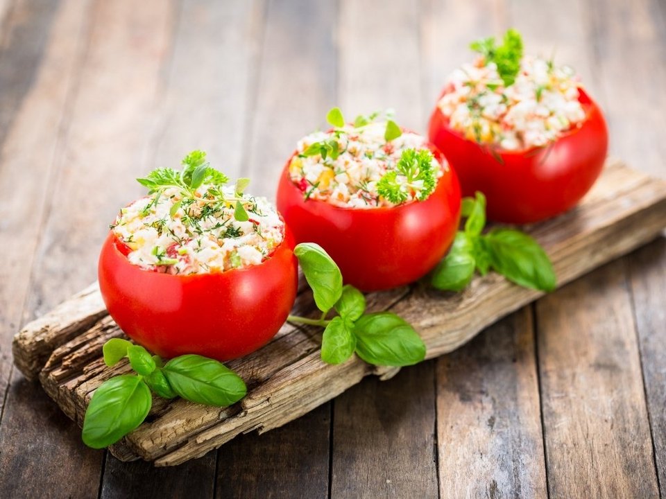 Trois tomates farcies au fromage et herbes, posées sur une planche en bois avec basilic frais, sur fond rustique.