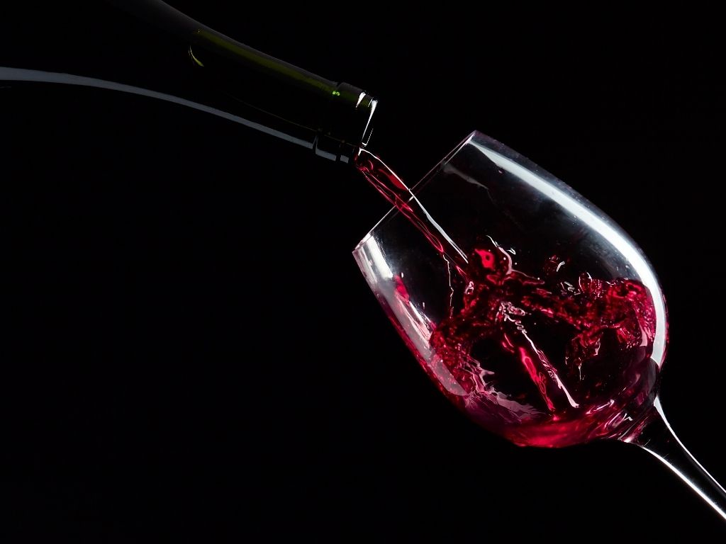 Vin rouge versé dans un verre sur fond noir, avec un mouvement net du liquide.