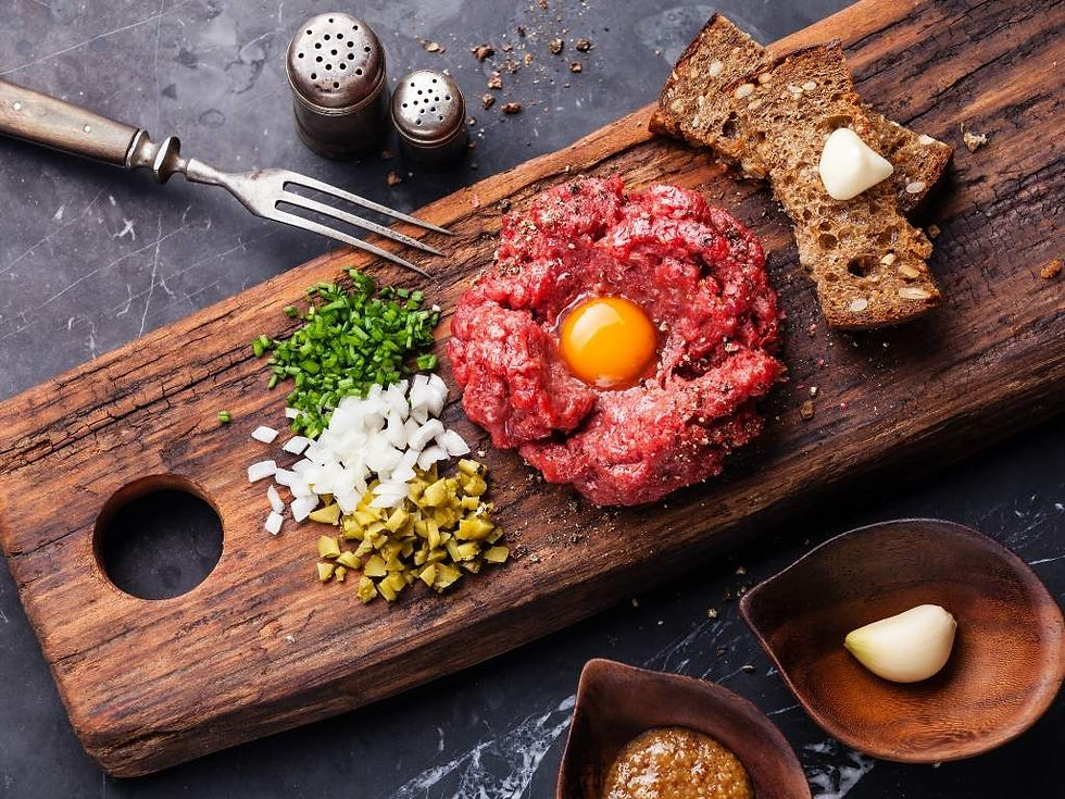 Tartare de bœuf avec jaune d'œuf sur planche bois, oignons, cornichons, ciboulette, pain, ail, sel, poivre. Fond marbre gris.