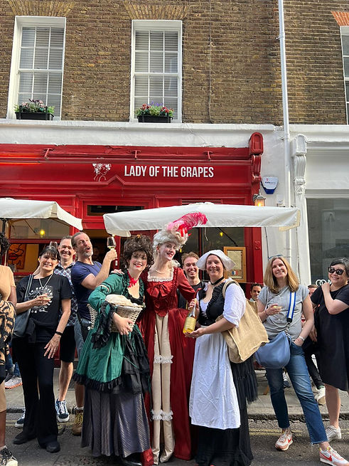 Photo of tour guide and actors in period costume standing in front of a wine bar with the group holding drinks