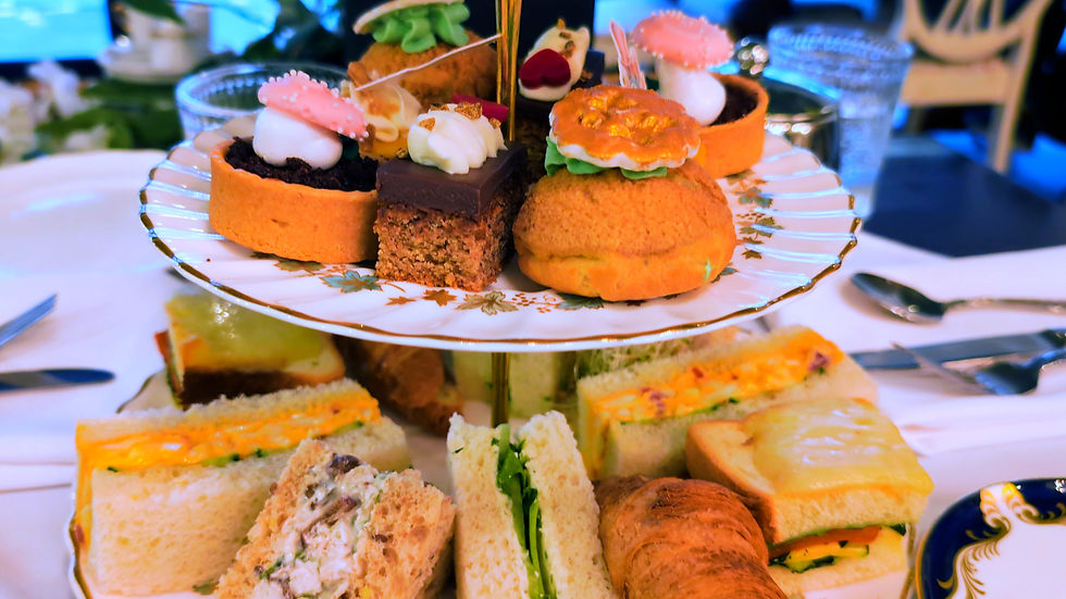 Tiered tea tray with decorated pastries and finger sandwiches on a white tablecloth, at a formal afternoon tea setting