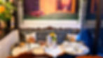 Whimsical tea party table with rabbit pillows, yellow rose, teacups, plates and menu reading Margherita in a cozy lounge.