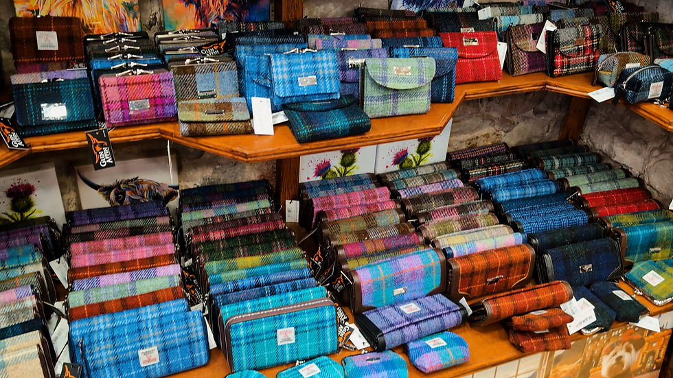 Rows of colorful plaid wallets and purses on wooden shelves in a shop, with price tags and Glen Cairn labels.