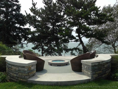 custom stone patio with curved seating walls and fire pit overlooking waterfront in Newton Massachusetts