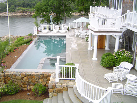 custom infinity pool with stone pool surround, granite patio, granite steps, retaining wall, and waterfront landscape installation in Massachusetts