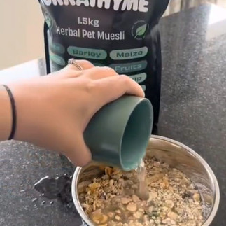 A bag of Tukkathyme Muesli with a dog owner pouring a cup of warm water over a bowl of Tukkathyme Original Formula dog muesli.