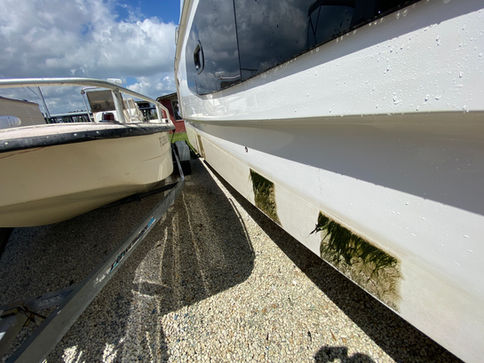 Thick green algae buildup in two streaks along the hull of an Aquila catamaran, caused by prolonged dockside storage.