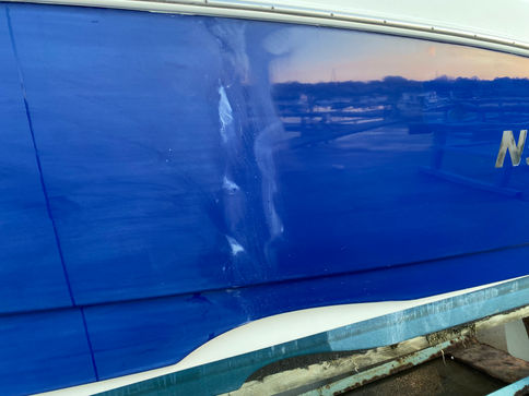 In-progress photo of a blue NauticStar Lowrider boat hull, showing heavy oxidation on the front half that still needs restoration.
