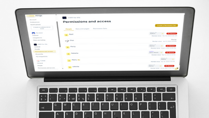 Workspace setup with a laptop displaying the Hylark “Permissions and access” dashboard. A coffee cup with latte art, a coiled black cable, and a notepad surround the laptop.