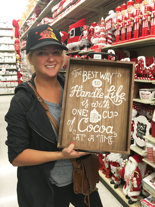 Emily Cameron holding a decorative sign in a home decor aisle