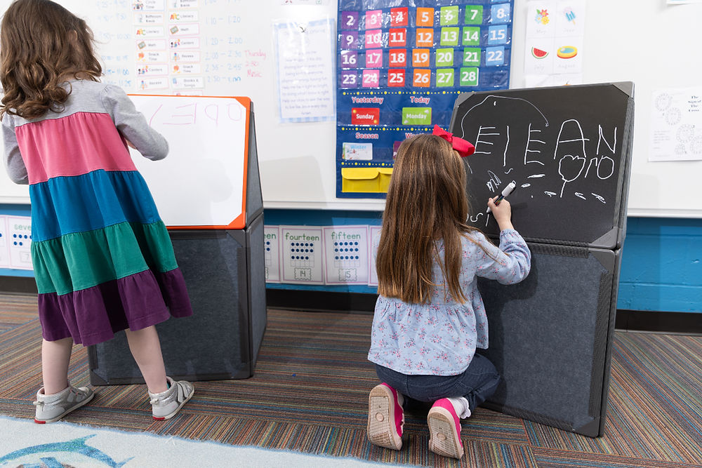 Children practice early writing and mark-making on Superspace's chalkboard and whiteboard panels - supporting emergent literacy, fine motor development, and creative expression within the classroom environment.