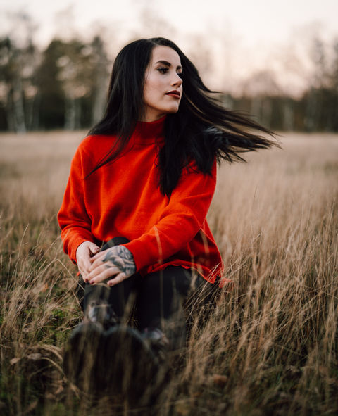 Selbstbewusstes Frauenporträt mit rotem Pullover im Feld sitzend von Ines Nienhaus Portraitfotografin