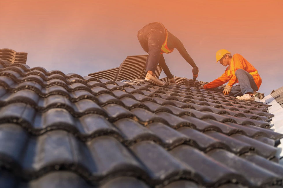 Two construction workers wearing high-visibility gear install dark ceramic roof tiles on a pitched roof using power tools.