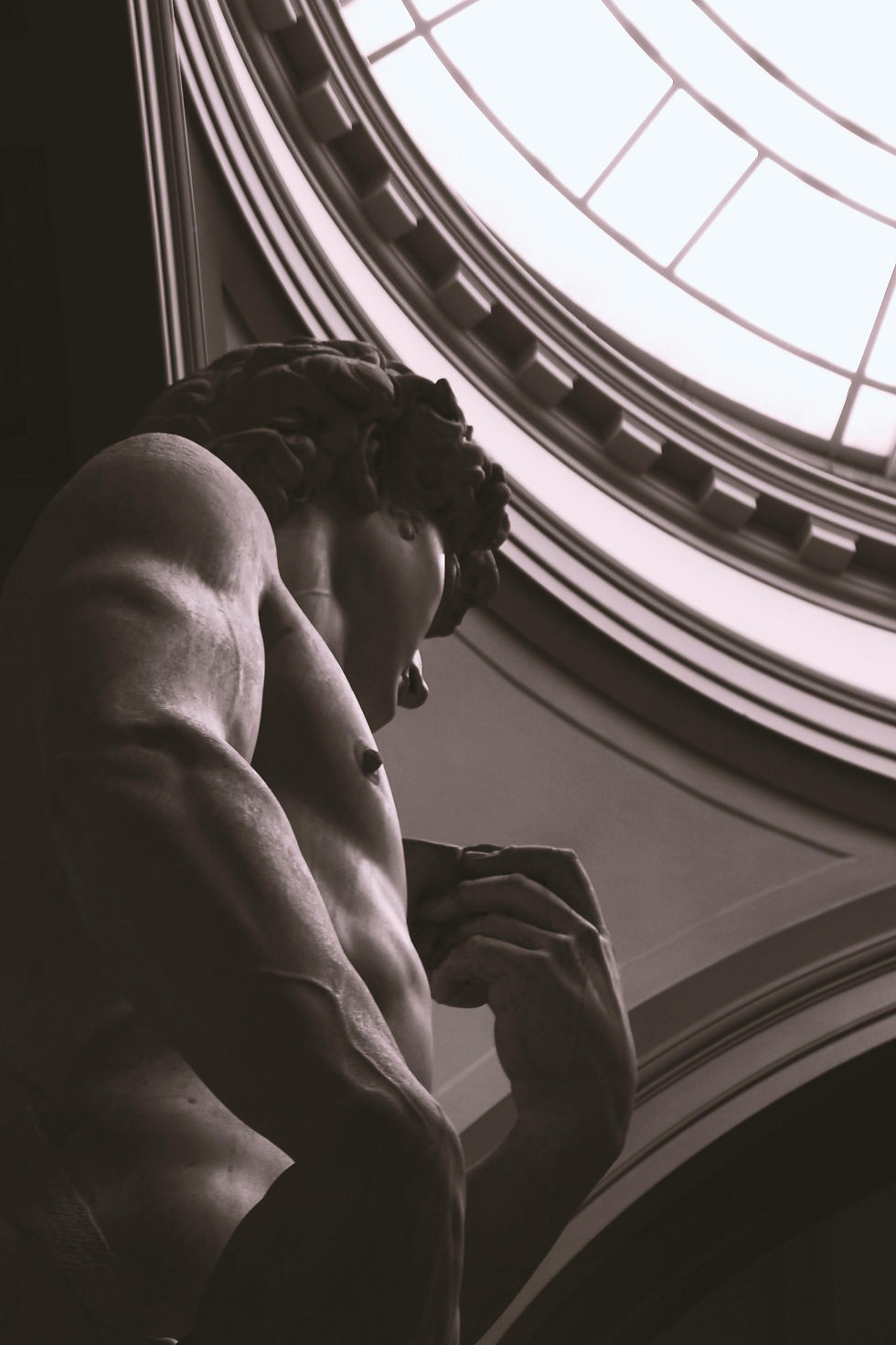 Stone statue of a scholar seated before a neoclassical building symbolizing learning and reason.