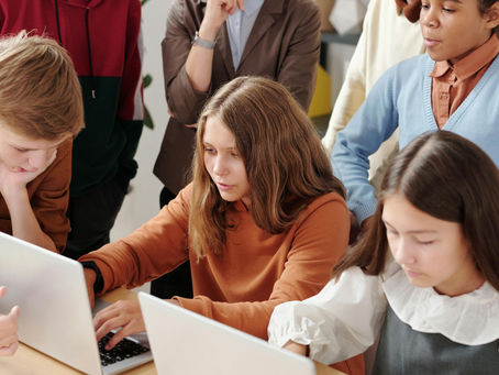 A diverse group of focused secondary school students collaborating on laptops in a modern classroom setting while a teacher observes, representing the shift toward competency-based learning in the CBSE Global Curriculum 2026.