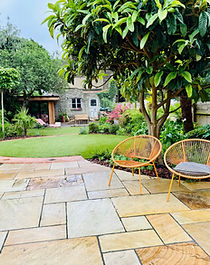 Stone patio with orange chairs overlooking curved lawn areas and lush planting.