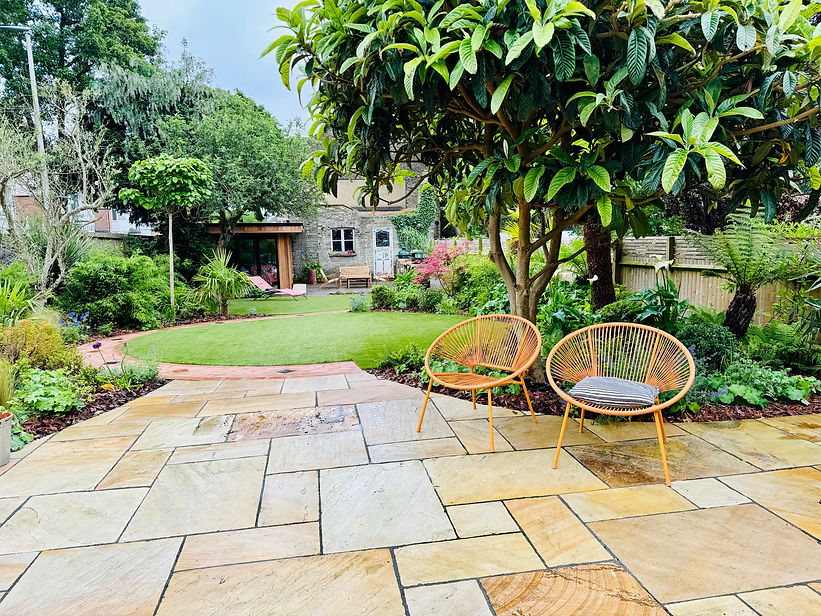 Stone patio with orange chairs overlooking curved lawn areas and lush planting.