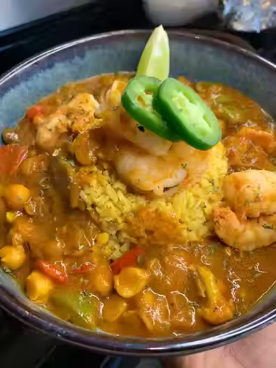 shrimp curry in a bowl with rice , topped with shrimp, jalapeno, and lime