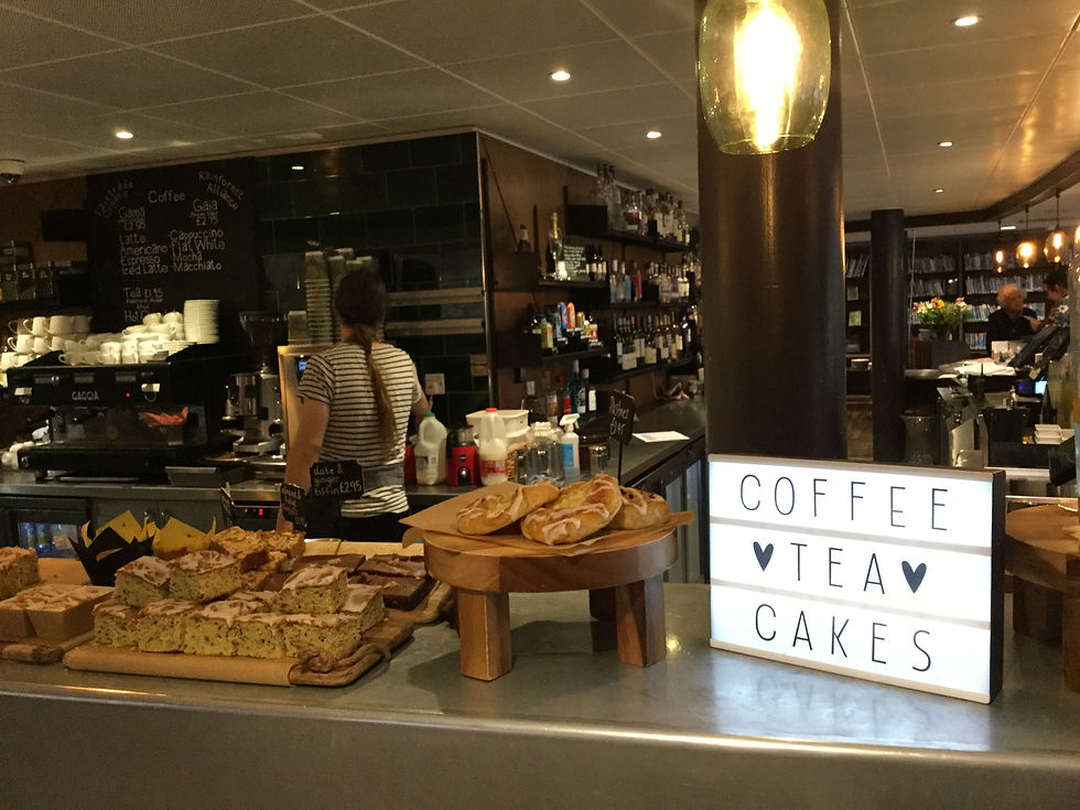 Croissants and pastries on the counter at a cafe serving area in the atrium of the Storyhouse. A light box with the words "Cofee, Tea, Cakes" on the front of it is shining in the foreground.