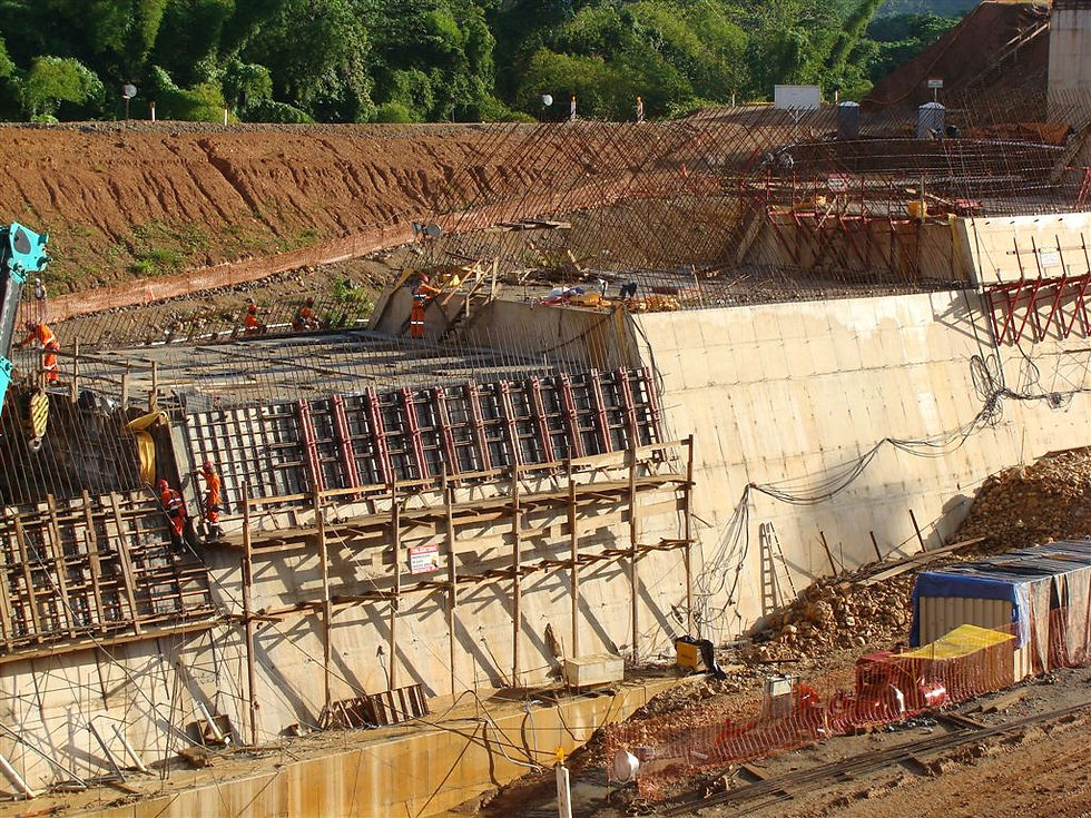 Construção de canal de concreto com formas posicionadas verticalmente e trabalhadores distribuídos ao longo da estrutura, com vegetação ao fundo.